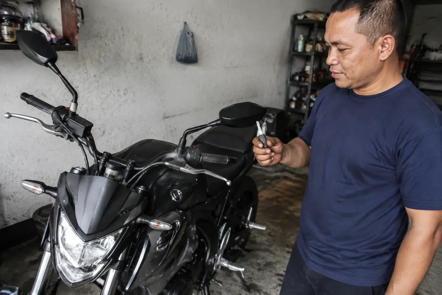 Person holding a key beside a black motorcycle in a garage. — Motorcycle & Scooter Keys, Richmond Hill