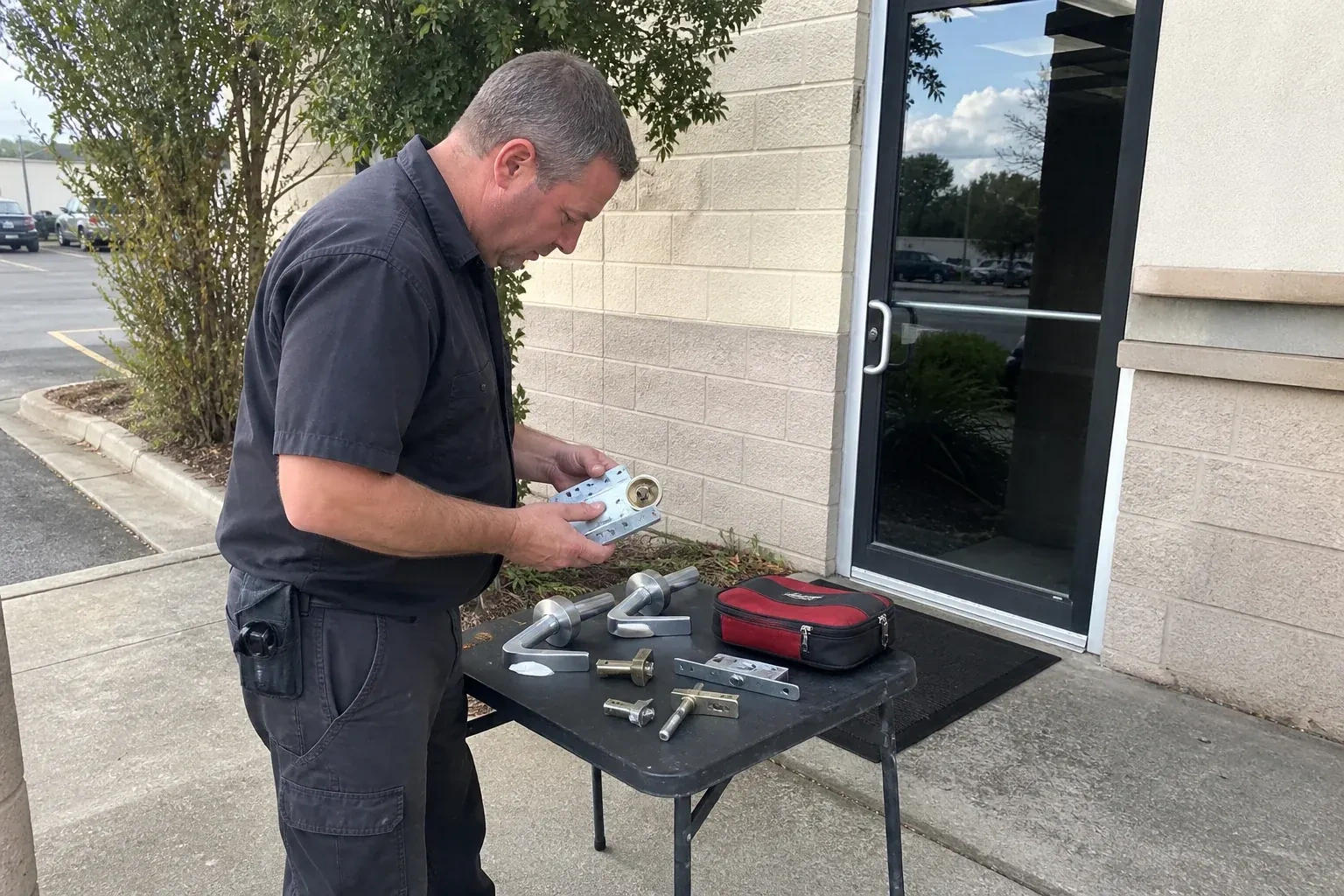 Technician examining detached commercial lock hardware on a table outside a shop entrance. — Business Lockout Service, Richmond Hill